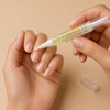 Person applying trooth beauty cuticle pen made with jamaican black castor oil to nails with a small applicator on a beige background